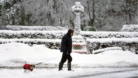 Owen Humphreys/PA A man walks his dog through snow-covered roads in Allenheads, Northumberland.