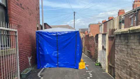 BBC/Yunus Mulla A blue forensic tent at the back of a terraced house 