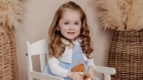 A young girl with brown hair smiling at camera