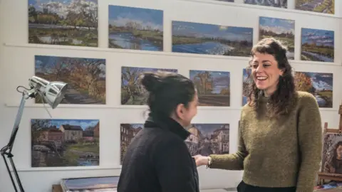 Sarah Allbrook Sarah Allbrook during Cambridge Open Studioss with artwork behind and talking to a member of the public