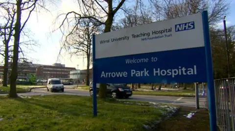 A blue and white NHS sign at the entrance to hospital grounds; the sign reads 'Welcome to Arrowe Park Hospital' 