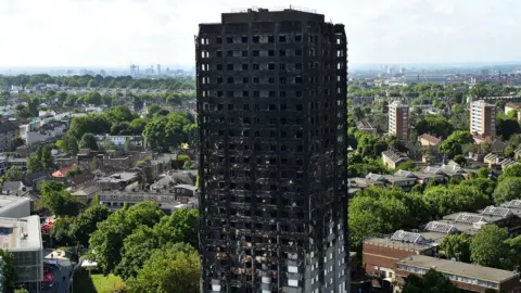 AFP The charred remains of Grenfell tower, West London, as seen from a height, with a panorama of leafy West London behind it.