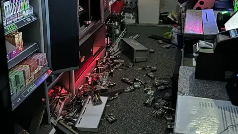 Susan Connolly Packets of cigarettes are visible discarded on the floor of a shop, behind the till.