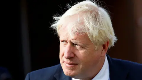 PA Media Boris Johnson pictured outside in the sunlight. He is wearing a suit and is squinting slightly looking off to his right.