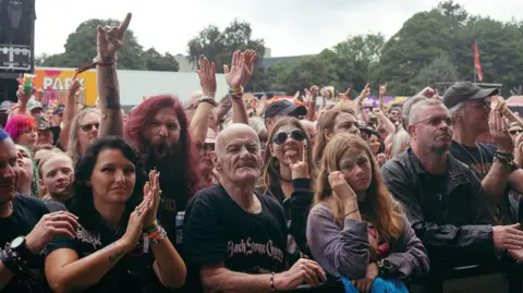 Maid of Stone Music fans standing at the front of a crowd, looking past the camera.