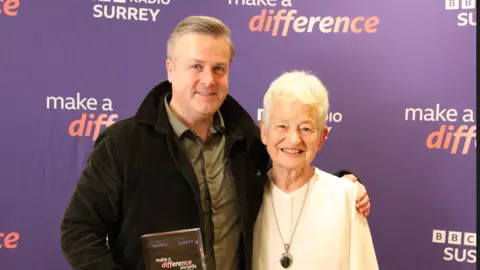 Chris Waller and Dame Jacqueline Wilson are standing in front of a purple backdrop