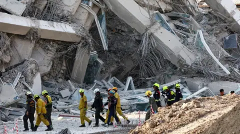 Reuters The rescuers wearing hard hats and protective overalls walk past huge blocks of rubble.