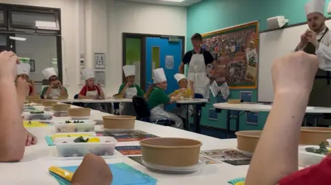 Children who listen to the professional chef talk about seasoning and the types of vegetables that can be used in cold salad.