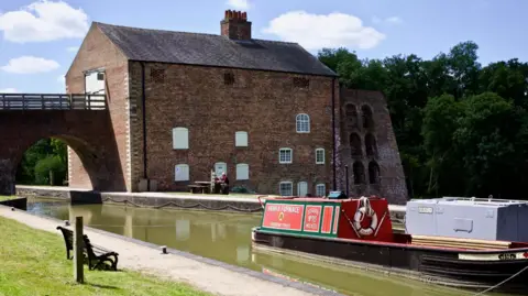 A large brick building next to a canal with a red boat on it