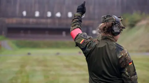 Getty Images A German drill instructor at a firing range holds up her left arm