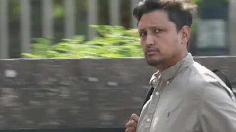 A man walks quickly past a camera. 