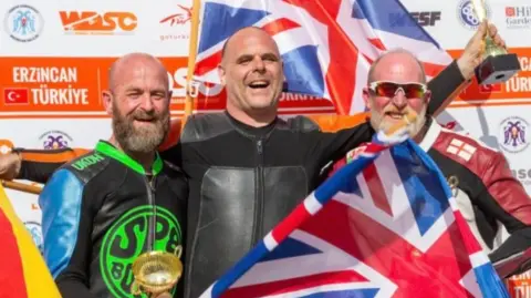 Mr Spencer with fellow British competitor Ian Martland and Dutch competitor Ulrich Becker at last year's championship. They're holding flags and trophies.