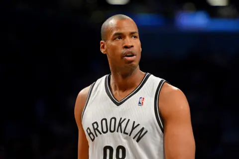 Jesse D. Garrabrant / NBAE via Getty Images Jason Collins is seen playing for the Brooklyn Nets in 2014. He is wearing a white NBA jersey that reads 'Brooklyn' and is exhaling while looking away from camera as he walks down the court against a black bokeh.