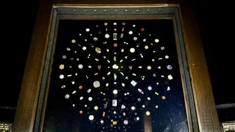  A framed display showing gems mounted in a circle, exhibited at Sotheby's