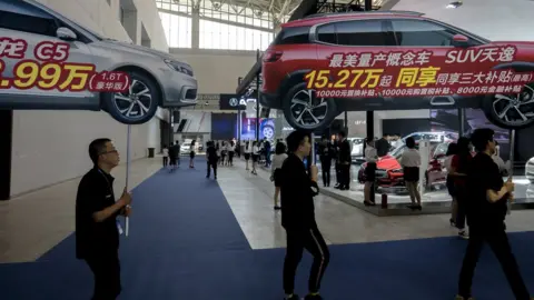 Getty Images Salesmen hold big car shape sales posters walking around, to attract customers on the Auto Expo.