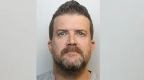 Man with beard and brown hair in a mugshot