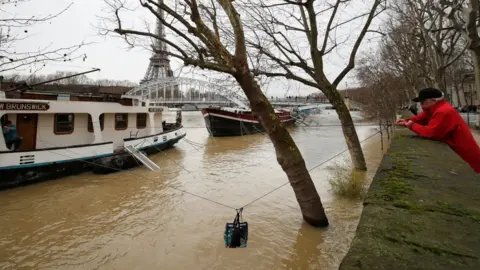 Reuters A man uses a rope to transfer a bag of supplies to his friend who lives on a houseboat as the banks of the Seine River are flooded after days of rain throughout the country and in Paris, France 25 January 2018 .