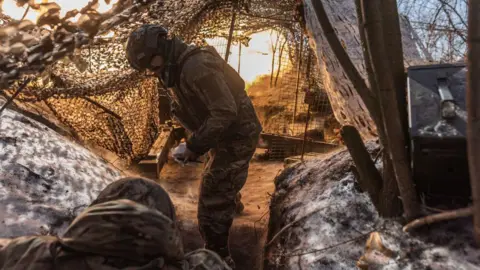 Getty Images A Ukrainian national guard soldiers stand in a trench under camouflage netting amid snowy conditions as they fire the Soviet D-20 artillery in the direction of Pokrovsk, Ukraine 