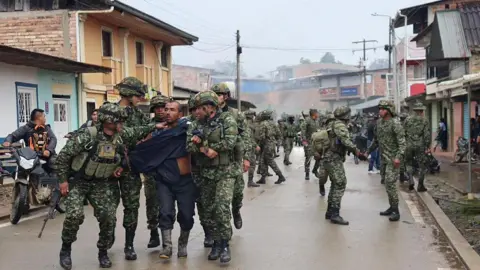Colombian Army/Handout via Getty A man is being escorted by soldiers in uniform in a street in El Tambo, Cauca. 
