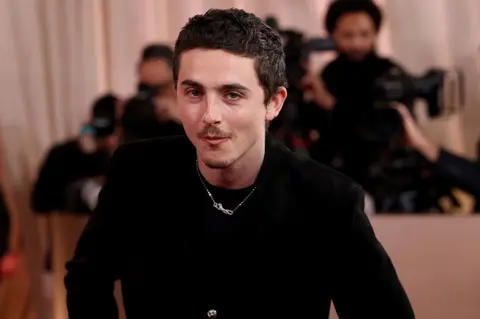 Getty Images Timothee Chalamet indossa un completo nero mentre posa sul tappeto rosso per l'83° Golden Globe Awards.