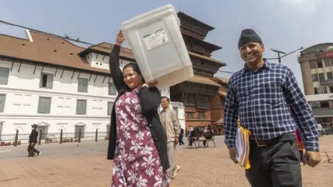 Nepalese election officers collect ballot boxes and necessary materials for the Nepal election. They are pictured here outside the office, with the woman carrying a large box