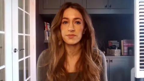 A woman with long wavy brown hair looks into the camera