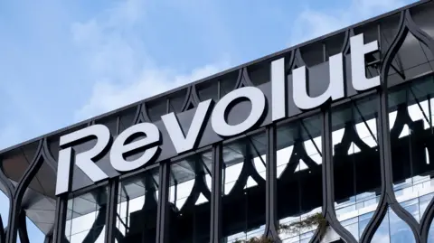 Getty Images A large glass fronted building with black metal framing sits in front of a blue sky. Writing on the building reads 'Revolut' in large white letters. 