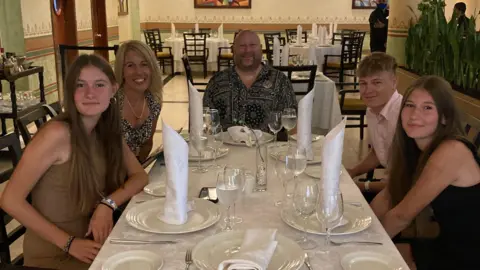 Melanie Goddard Ethan Goddard with his parents and twin sisters sitting round a table at a restaurant