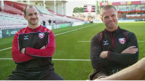 Gloucester Rugby players Tomas Williams and Gareth Anscombe sitting on the pitch at Kingsholm Stadium