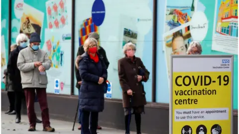 Reuters People queue to receive the coronavirus vaccine outside a closed down Debenhams store that is being used as a vaccination centre in Folkestone, Kent