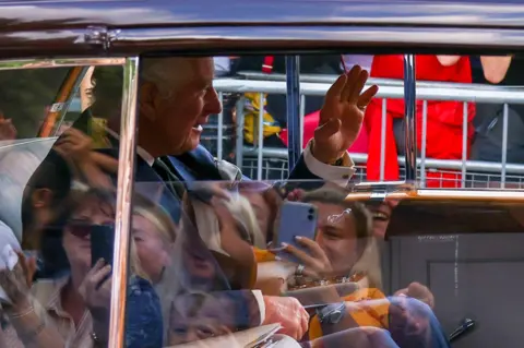 Henry Nicholls/ Reuters The King waves to crowds as he arrives as Buckingham palace