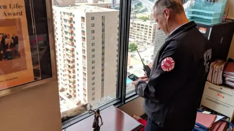 Tim Nelson/ MPR News A fire official takes photograph of raccoon through glass