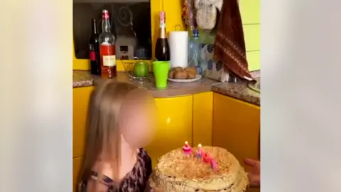Ukrainian armed forces/Telegram Girl (face blurred) blows out candles on a birthday cake in yellow kitchen