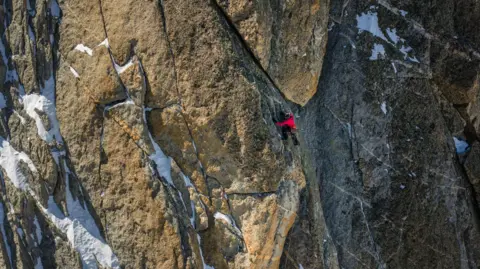 Jan Virt A drone image of Fay Manners ascending Tête Biselx. Parts of the mountain are covered in snow.