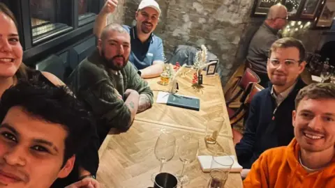 Dean Perryman A group at a pub smile at the camera. Dean Perryman is at the bottom right of the image wearing an orange hoodie