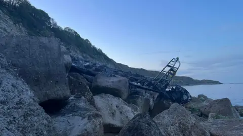 Swanage Coastguard Charred wreck of boat beached on large rocks