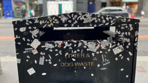 A litter and dog waste bin is covered with small sticky tabs which form the seals of disposable vapes.