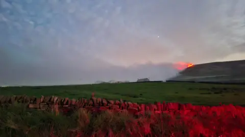 WYFRS A large fire with billowing smoke on moorland with a house in the distance.
