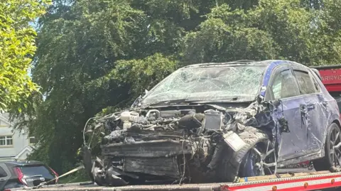 A smashed navy Volkswagen Golf car sitting atop a tow truck. 