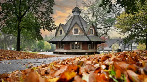 Bournville Village Trust A hexagonal building with a triangular roof in the middle of a park with red autumn leaves all around