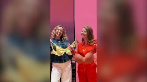 Nuala McGovern and Katie Weir stand side by side each holding a bra. They both smile at the camera.