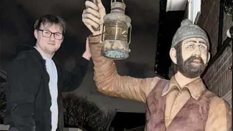 Kyle Wilcock with his left hand is touching the right arm of the statue