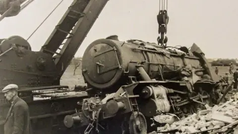 The Cambridgeshire Collection Aftermath of Soham rail disaster, 1944 - a wagon train sits at a tilt amid rubble - photo is black and white 