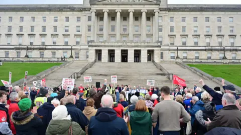 Pacemaker A large group of campaigners standing in front of the footsteps of Stormont. 