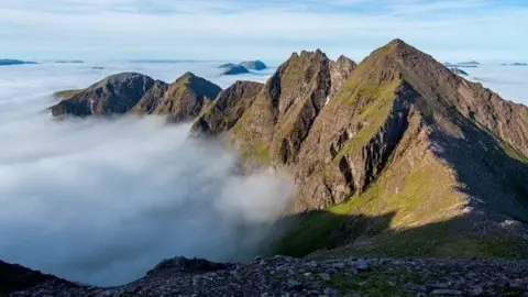 LITTLEHOUSE MEDIA A rugged mountain landscape with clouds around the peaks of a Highland range