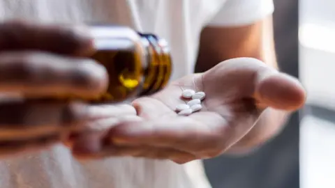 Getty Image Person with a brown bottle and white pills in the palm of his hand