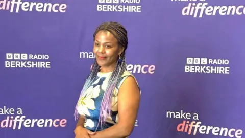 Tutu Melaku Tutu is standing behind a Make A Difference Award billboard 
