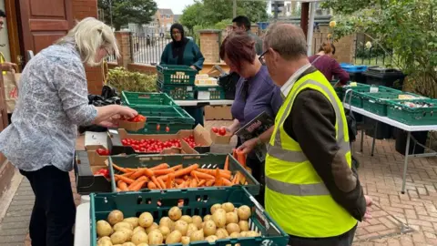 London's Community Kitchen Staff at London's Community Kitchen sort piles of red tomatoes, orange carrots and potatoes into green trays on trestle tables