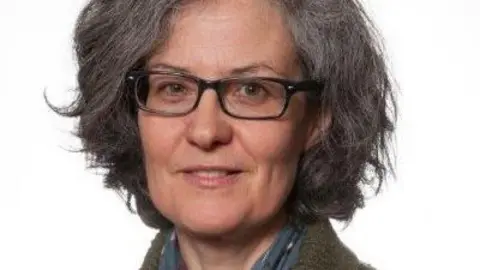 University of Chester A woman with a grey-brown bob and square black glasses smiles at the camera in a professional portrait