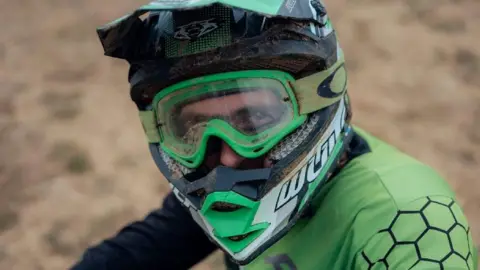 Harry George Hall A driver in green racing wear including a green helmet - behind the visor he is looking straight at us